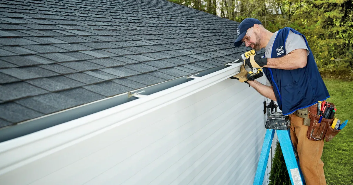 Technician installing a seamless gutter system along a building roofline